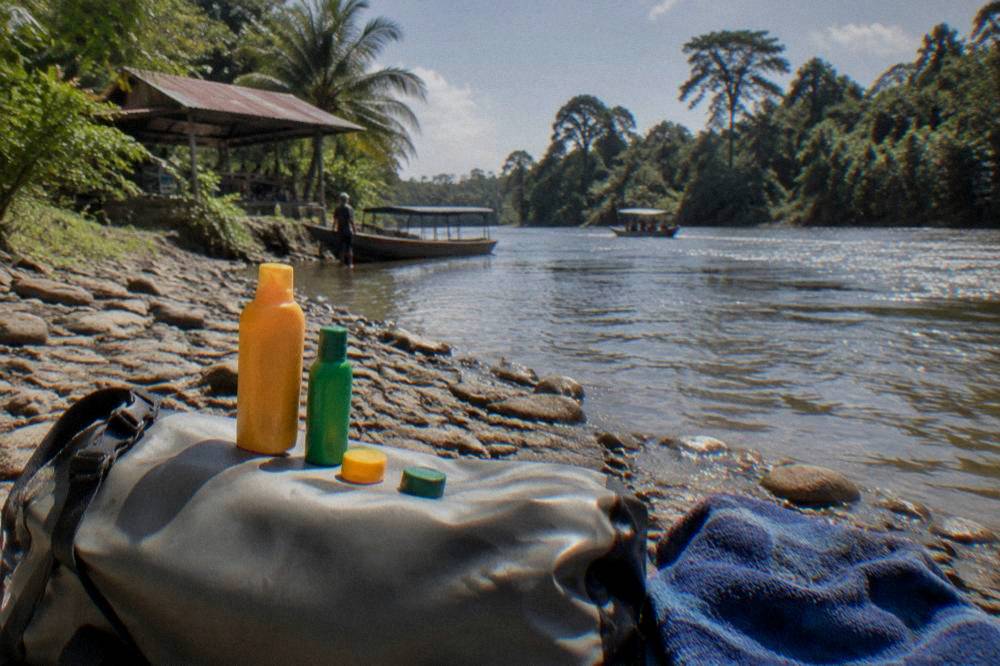 Sunscreen and insect repellent bottles resting on a dry bag beside a river