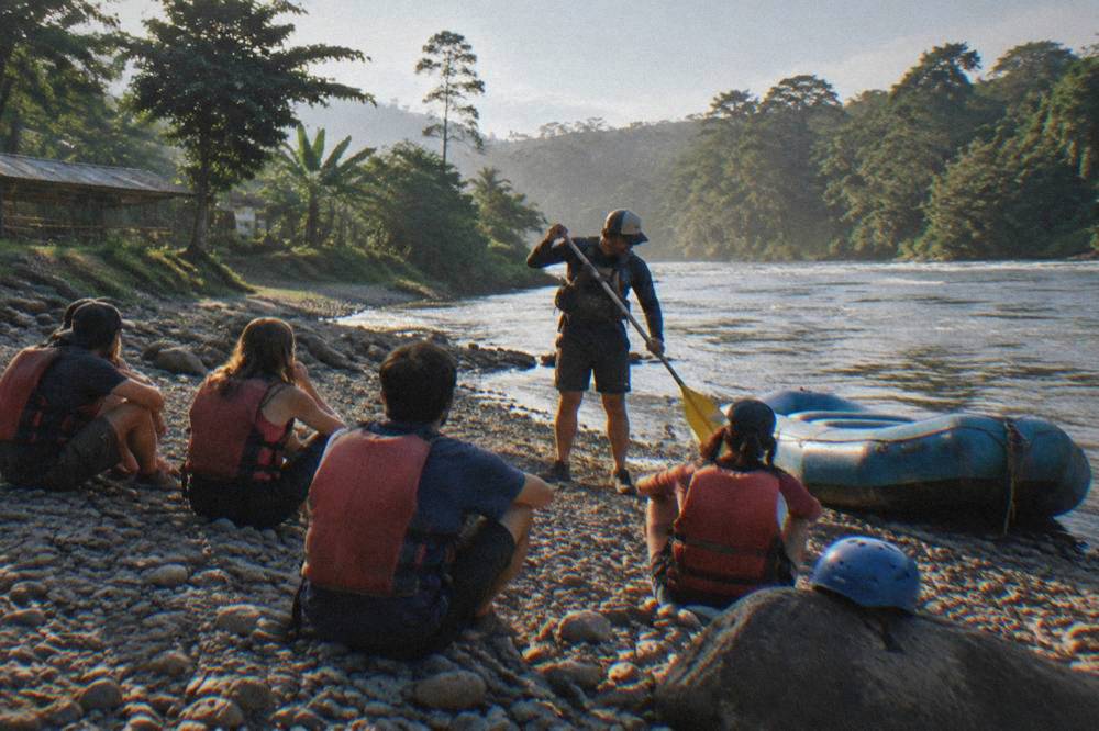 A guide demonstrating paddle strokes to a raft crew on a riverbank